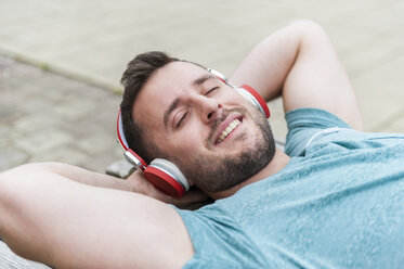 Relaxed young man lying on bench listening to music - DIGF000700