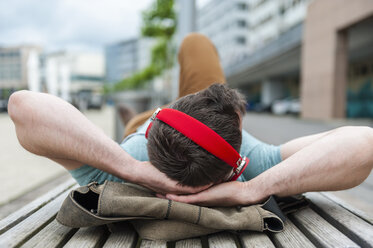 Relaxed young man lying on bench listening to music - DIGF000701