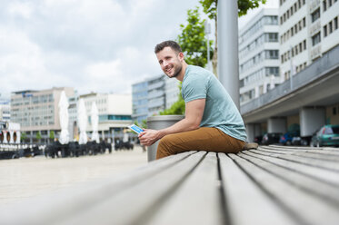 Smiling young man outdoors sitting on bench with digital tablet - DIGF000703