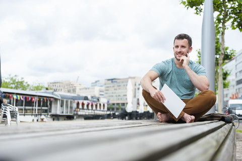 Relaxed young man outdoors sitting on bench with digital tablet stock photo