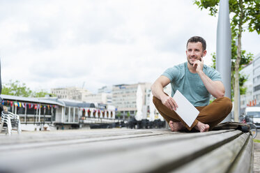 Relaxed young man outdoors sitting on bench with digital tablet - DIGF000704