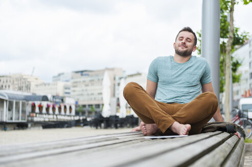 Entspannter junger Mann im Freien auf einer Bank sitzend - DIGF000705