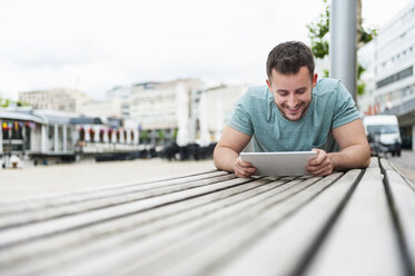 Lächelnder junger Mann im Freien auf einer Bank liegend mit einem digitalen Tablet - DIGF000706