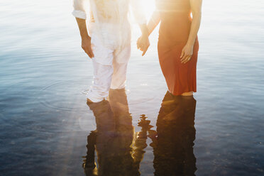 Händchenhaltendes Paar, im Wasser stehend, gegen die Sonne - MJF001990