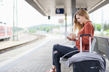 Junge Frau sitzt auf einer Bank am Bahnsteig und benutzt ein Tablet - DIGF000716