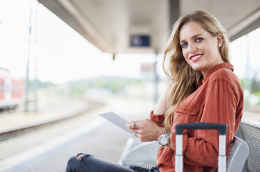 Porträt einer lächelnden jungen Frau mit Tablet, die auf einer Bank am Bahnsteig sitzt - DIGF000717