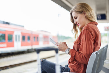 Junge Frau sitzt auf einer Bank am Bahnsteig und benutzt ein Tablet - DIGF000718