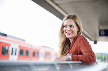 Porträt einer lächelnden jungen Frau, die am Bahnsteig sitzt - DIGF000720