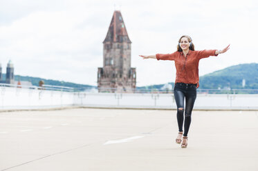 Germany, Saarbruecken, woman listening music with headphones dancing on roof terrace - DIGF000726