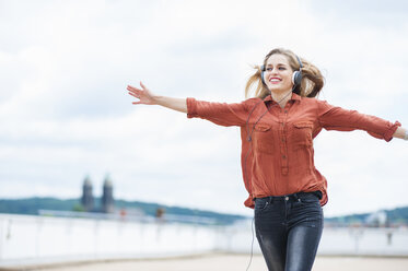 Happy woman with arms outstretched listening music with headphones - DIGF000727