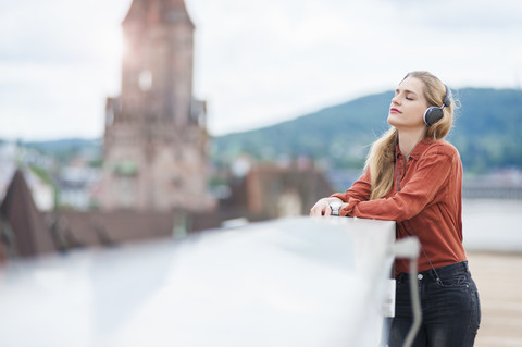 Deutschland, Saarbrücken, Frau hört Musik mit Kopfhörer auf Dachterrasse, lizenzfreies Stockfoto