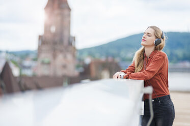 Germany, Saarbruecken, woman listening music with headphones on roof terrace - DIGF000729