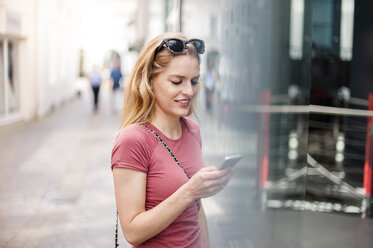 Young woman standing in front of shop window looking at her smartphone - DIGF000739