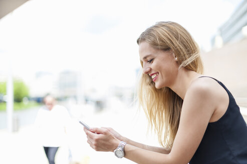 Lächelnde junge Frau schaut auf ihr Handy - DIGF000752