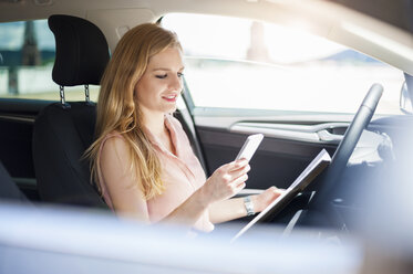 Junge Geschäftsfrau sitzt in ihrem Auto und schaut auf ihr Mobiltelefon - DIGF000756