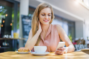 Porträt einer lächelnden Frau, die in einem Straßencafé sitzt und auf ihr Smartphone schaut - DIGF000760