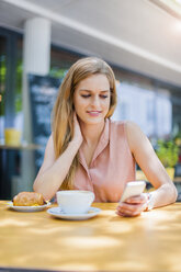 Porträt einer lächelnden Frau, die in einem Straßencafé sitzt und auf ihr Smartphone schaut - DIGF000761