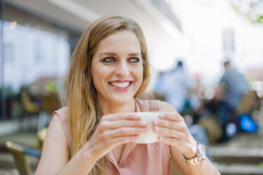 Porträt einer lächelnden Frau, die in einem Straßencafé mit einer Tasse Kaffee sitzt - DIGF000762