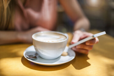 Frau sitzt in einem Café mit Cappuccino und hält ihr Smartphone, Nahaufnahme - DIGF000763