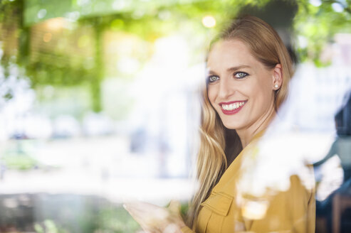 Porträt einer lächelnden Frau, die hinter dem Fenster eines Cafés sitzt - DIGF000765