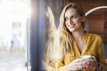 Porträt einer lächelnden Frau in einem Café, die durch ein Fenster schaut - DIGF000766