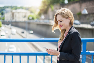 Lächelnde Geschäftsfrau auf einer Brücke, die auf ihr Smartphone schaut - DIGF000768