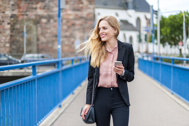 Smiling businesswoman walking on a bridge looking at her smartphone - DIGF000769