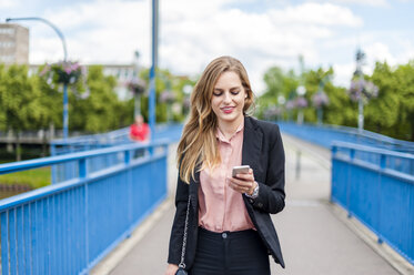 Lächelnde Geschäftsfrau auf einer Brücke, die auf ihr Smartphone schaut - DIGF000770