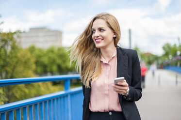 Smiling businesswoman on a bridge with smartphone - DIGF000771