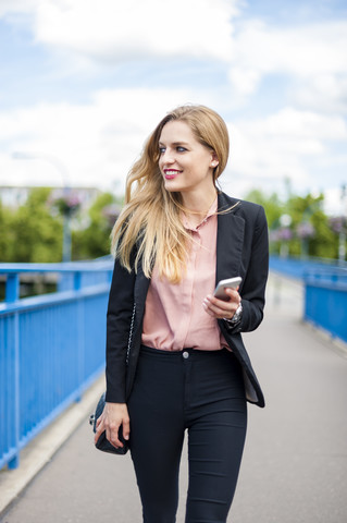 Smiling businesswoman walking on a bridge holding smartphone stock photo