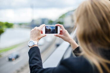Rückansicht einer Frau, die auf einer Brücke steht und ein Foto mit ihrem Smartphone macht - DIGF000773