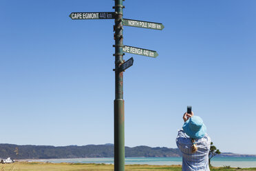 New Zealand, North Island, East Cape, woman taking smartphone photos of signposts in Te Araroa - GWF004804