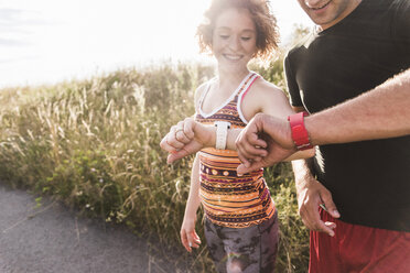 Sportive young couple in field looking at watches - UUF008095