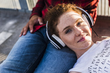 Junge Frau mit Kopfhörern auf dem Schoß ihres Freundes liegend - UUF008115