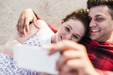 Smiling young couple lying down taking a selfie - UUF008118