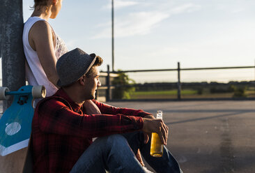 Junges Paar mit Skateboard und Bierflasche genießt den Sonnenuntergang - UUF008124