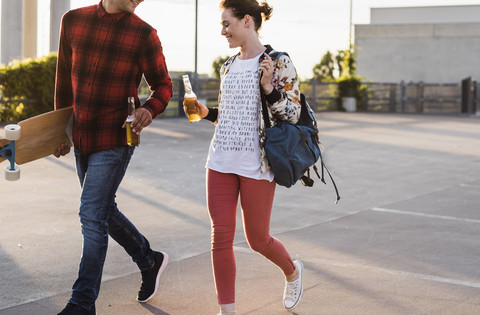 Junges Paar mit Bierflaschen und Skateboard zu Fuß im Freien, lizenzfreies Stockfoto