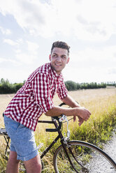 Lächelnder junger Mann mit Fahrrad in der Natur - UUF008138