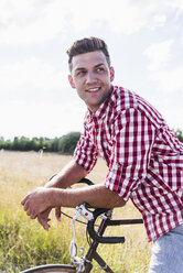 Lächelnder junger Mann mit Fahrrad in der Natur - UUF008139