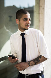 Porträt eines jungen Geschäftsmannes mit Smartphone, der in die Ferne schaut - GIOF001256