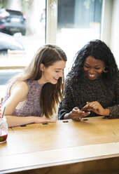 Zwei junge Frauen benutzen ein Smartphone in einem Café - ONF000963