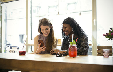 Junge Frauen in einem Café schauen auf ihr Smartphone - ONF000964