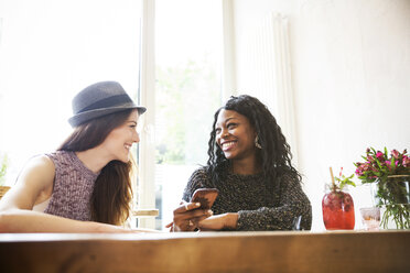 Junge Frauen in einem Café schauen auf ihr Smartphone - ONF000968