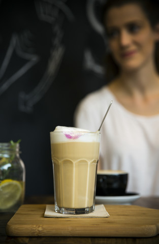 Glas Milchkaffee auf einem Tisch in einem Café mit einer jungen Frau im Hintergrund, lizenzfreies Stockfoto