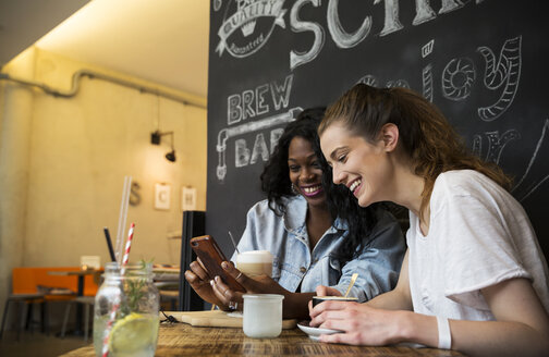 Zwei Freunde im Café schauen auf ihr Smartphone - ONF001001