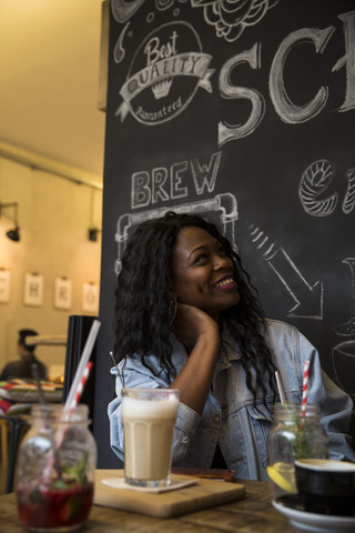 Junge Frau sitzt im Café mit einem Glas Milchkaffee, lizenzfreies Stockfoto