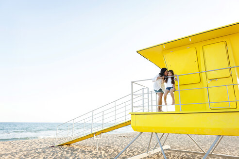 Mother kissing her little daughter on a yellow lifeguard stand - VABF000699