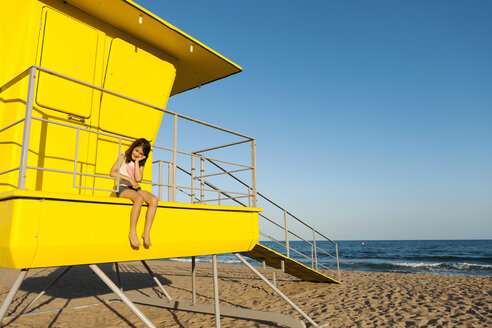 Kleines Mädchen sitzt auf einem gelben Rettungsschwimmerstand am Strand - VABF000700