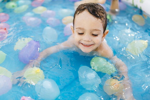 Lächelnder kleiner Junge spielt mit Wasserballons im Pool - JRFF000767
