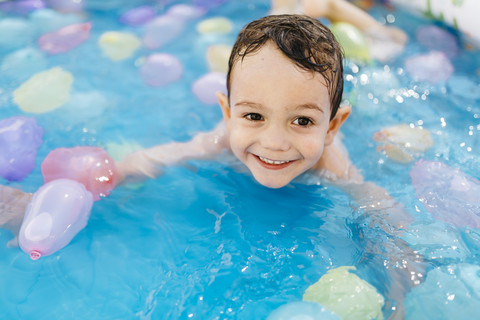 Lächelnder kleiner Junge spielt mit Wasserballons im Pool, lizenzfreies Stockfoto